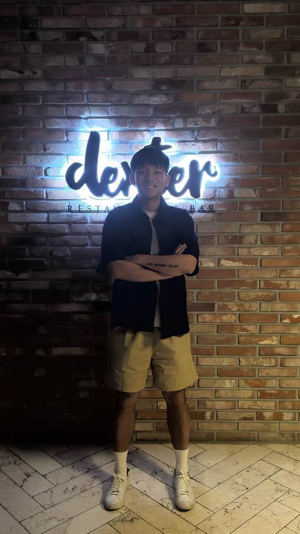 Dexter standing under a neon sign that reads dexter